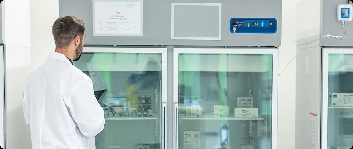 Scientist checking medical supplies in a temperature-controlled lab refrigerator.